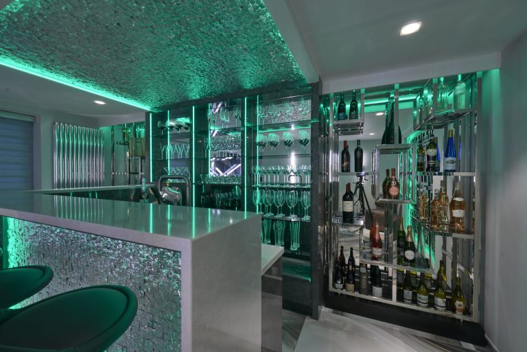 Bar and wine display lit blue in a basement entertaining space