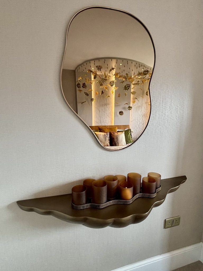 Abstract mirror above an organic shaped console table with candles