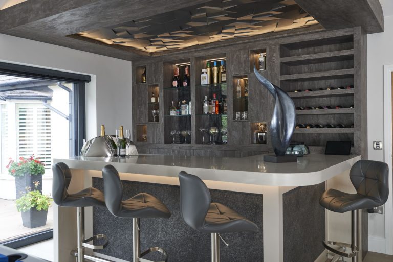 Bar built into the end of a kitchen with lit shelving and stools