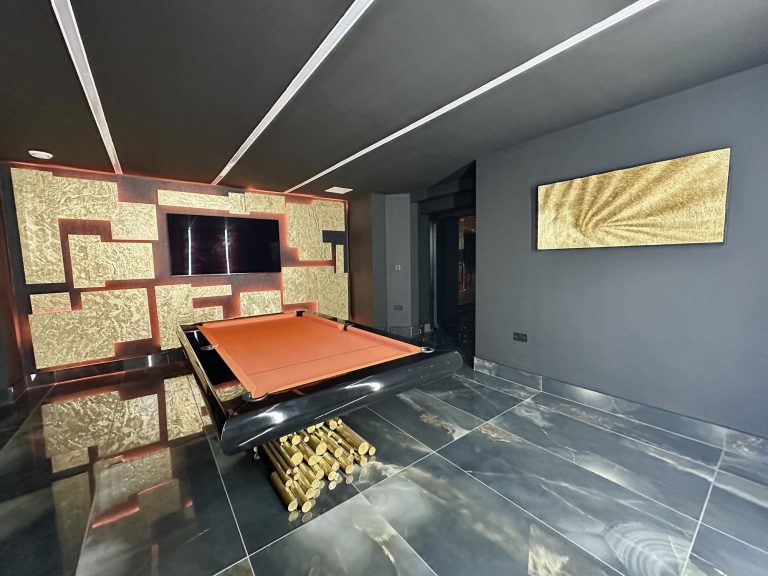 Media wall in backlit gold leaf panels above a pool table in a games room