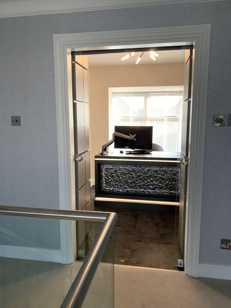 Fitted study desk with a lit textured panel, seen through a glass door from the landing
