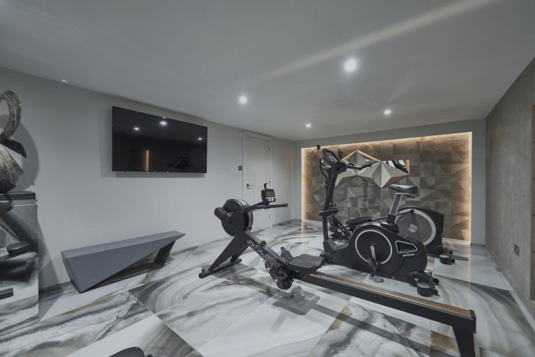 Home gym with a rower and exercise bike below a wall hung screen