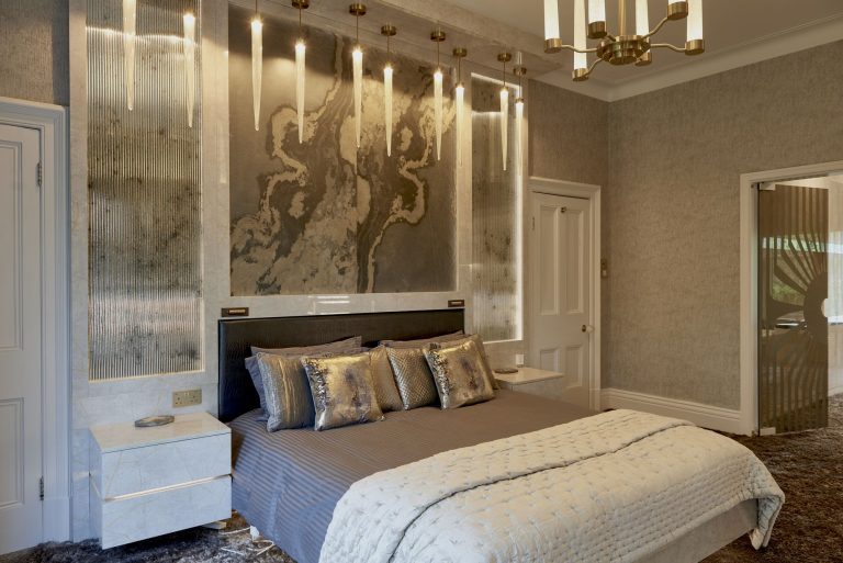 Bed against a bark and silver foil wall covering below lit panels