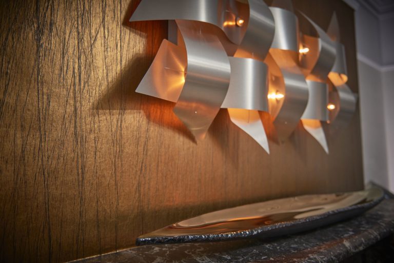 Metal wall sculpture lit against a textured gold panel