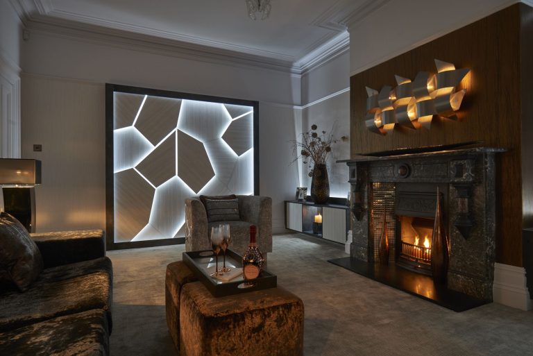 The lit panel and the metal wall sculpture above the fire