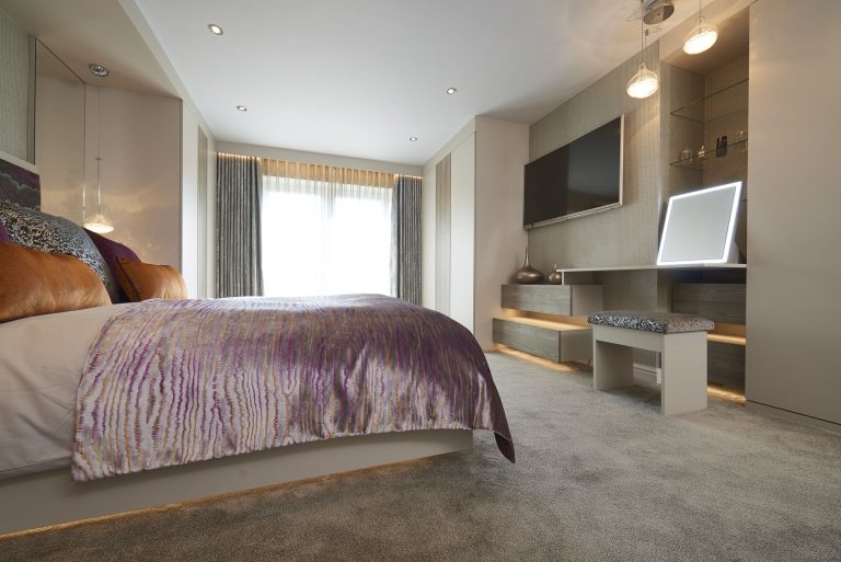 The bedroom towards a fitted dressing unit with a lit mirror and a wall hung screen