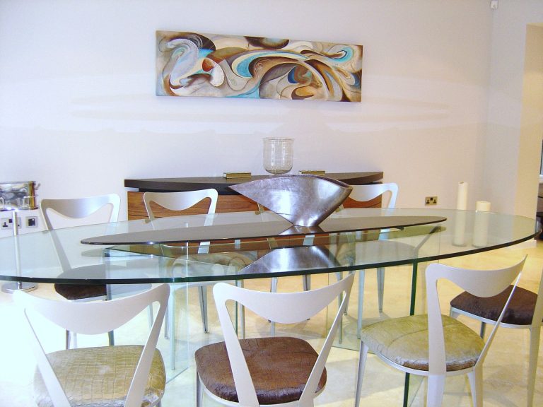 Oval glass dining table below original artwork