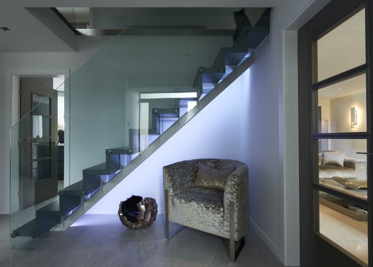 Glass balustraded staircase with a tub chair beneath it