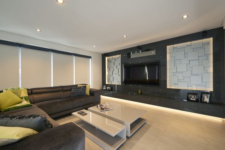 Open-plan living room with a backlit media wall and a grey corner sofa