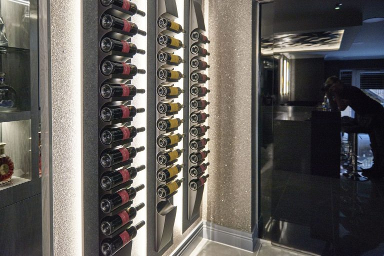 Wine bottles displayed in a lit wall rack beside the bar