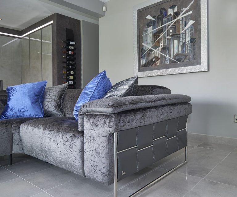 Corner sofa in navy and grey velvet with a wine display behind